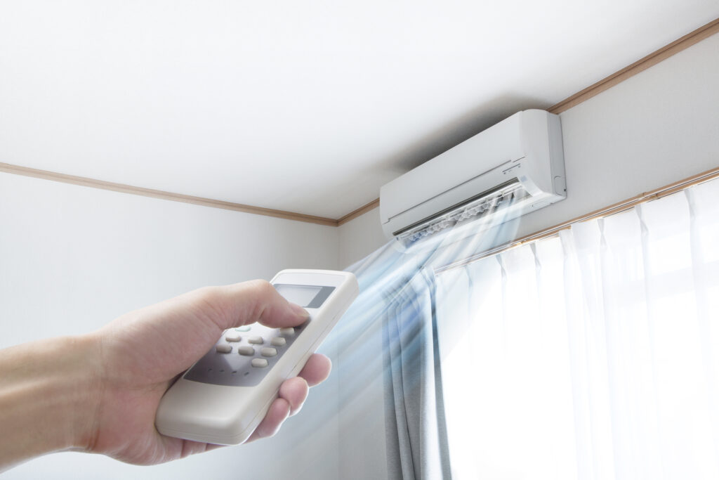 white ductless mini split mounted on the wall above a window with hand holding remote pointed at flowing air
