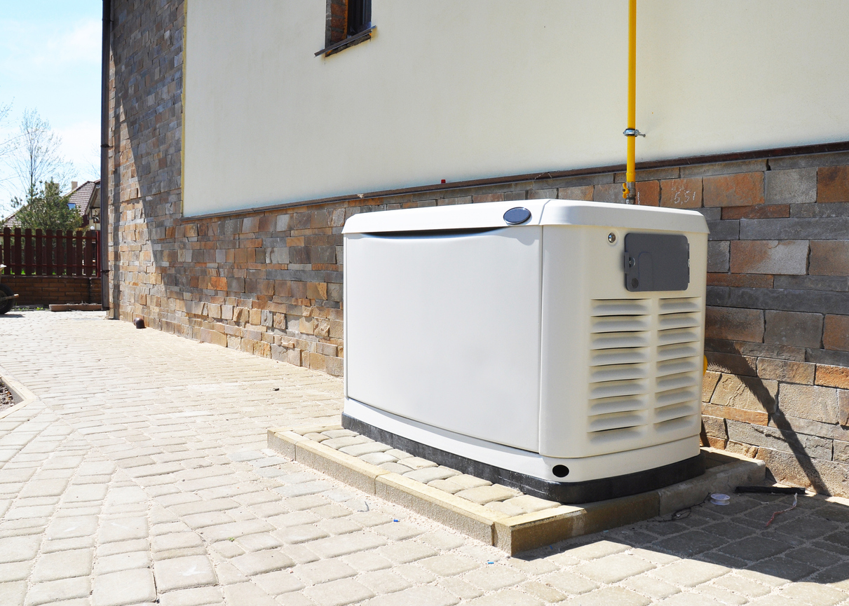 Residential generator installed outside of a white stucco-and-brick home.